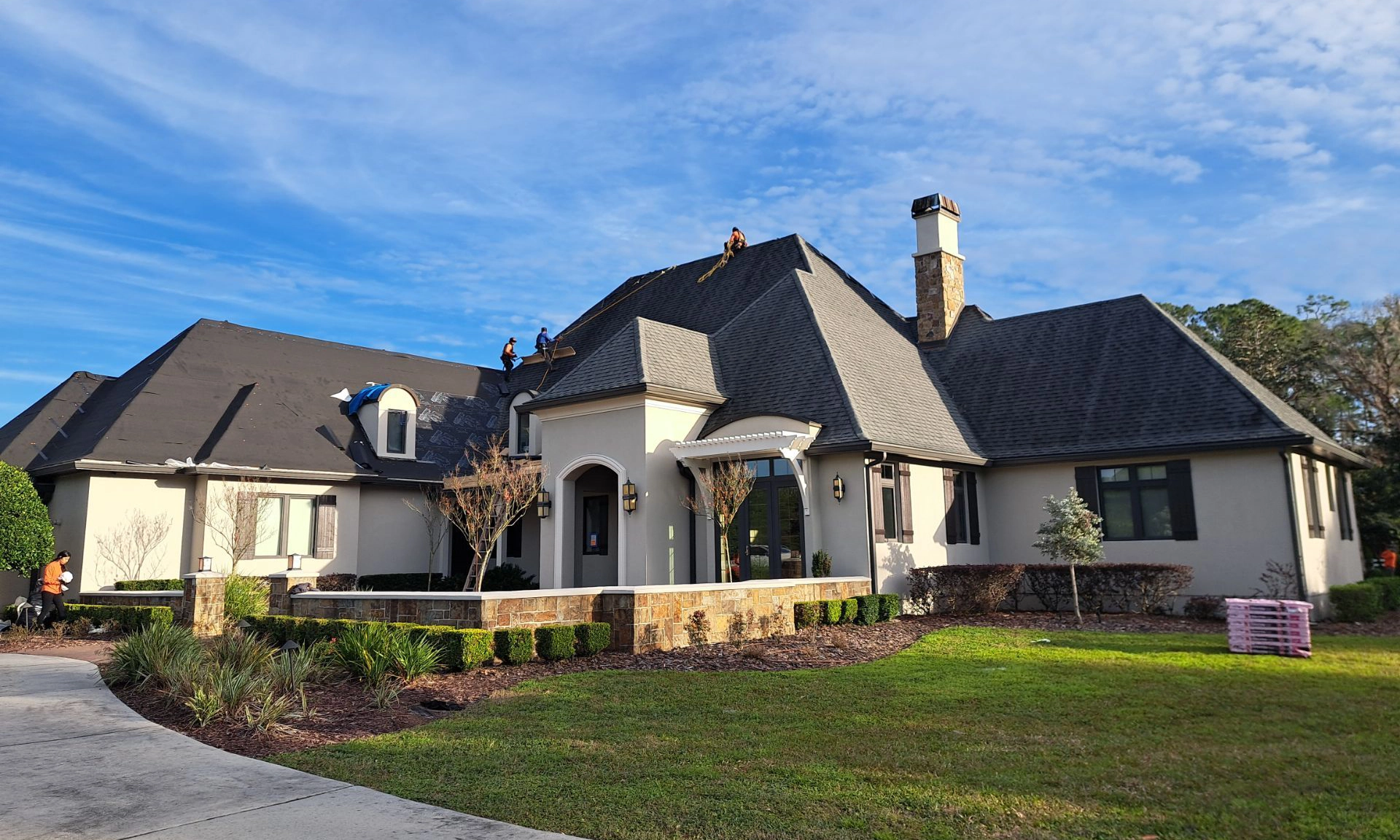 Roofers working on the installation of shingles on a high slope roof of a large house.