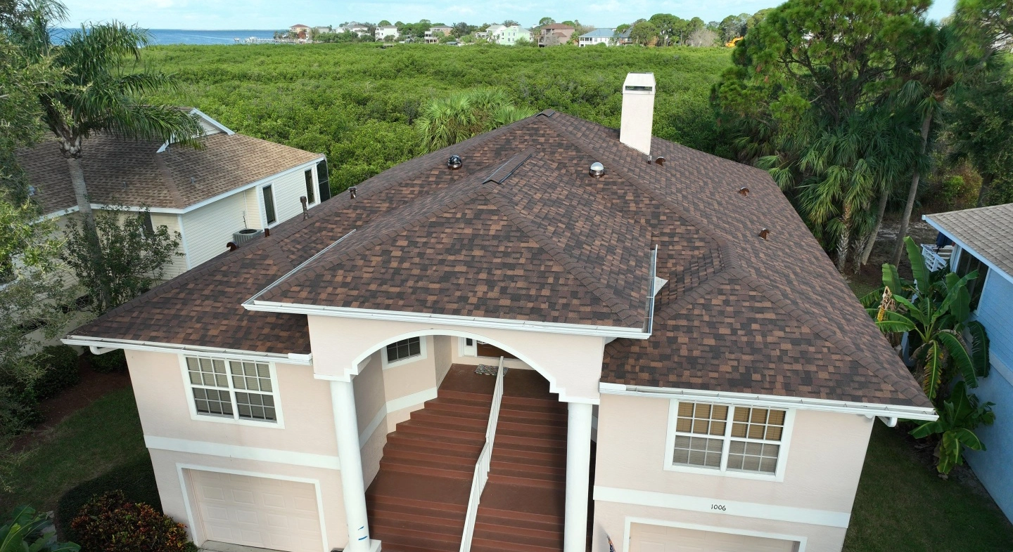 Completed shingle roofing on a stucco duplex with a brown roof and white exterior.